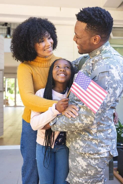A U.S. Army service member embracing his family, holding an American flag